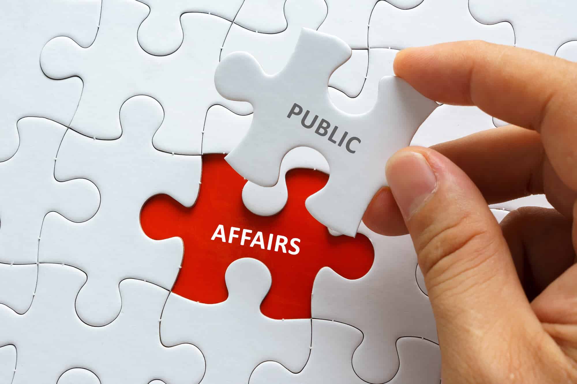 Hand holding piece of jigsaw puzzle with word PUBLIC AFFAIRS.
